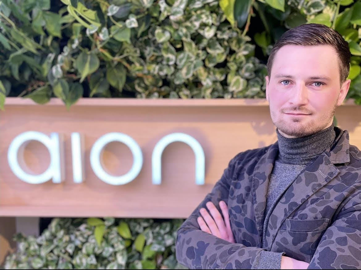 Image of a man standing in front of the Aion logo